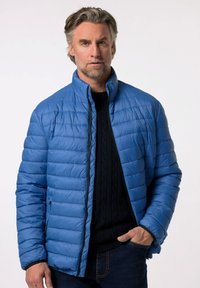 Modrá péřová bunda s horizontálním prošívaným vzorem, vysokým límcem a zipovým zapínáním. Nosit na tmavém pleteném svetru a džínech.