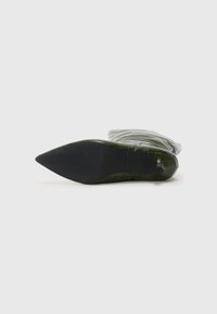 Stivale verde a punta, con suola texturizzata, sdraiato su un lato su uno sfondo bianco semplice.