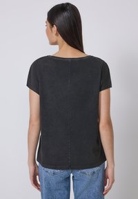 Sort t-shirt med korte ærmer, afslappet pasform, rund halsudskæring og subtil tekstur, båret med lyseblå højtaljede jeans.