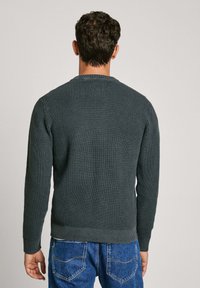 Donkergrijze gebreide trui met een gestructureerde afwerking, lange mouwen en een geribde zoom, gecombineerd met blauwe spijkerbroeken.