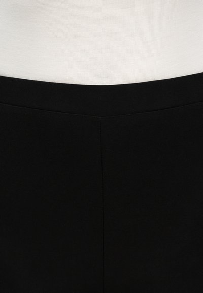 Κοντινό πλάνο μαύρης ζώνης μέσης και επάνω άκρου εφαρμοστών παντελονιών σε λευκό φόντο.