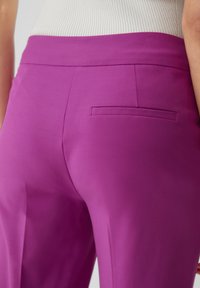 Pantalon ajusté violet avec une texture lisse, présentant une poche arrière unique et une ceinture au design épuré.