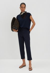 Haut marine à manches courtes, pantalon assorti et tongs noires. Une pochette en cuir brun texturé et un foulard en soie à motifs viennent compléter la tenue.