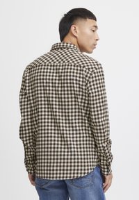 Camisa de cuadros marrones y blancos, con cuello clásico, mangas largas y dobladillo curvedo, fabricada en un tejido texturizado.