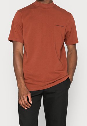 Rustfarvet t-shirt med korte ærmer lavet af bomuld, med høj krave og lille sort logo på brystet. Glat tekstur.