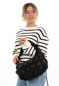 Black quilted handbag with a textured finish and large, twisted handle. Worn with a striped sweater and denim, highlighting modern design.