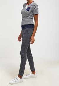 Randig kortärmad topp med röd halsringning och blå ficka, kombinerad med prickiga marinblå byxor. Modellen bär vita sneakers med kardborreband.