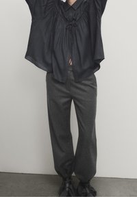 Zwarte linnen blouse met korte, brede mouwen en een strik bij de halslijn, gecombineerd met grijze tapered broek met elastische cuffs.