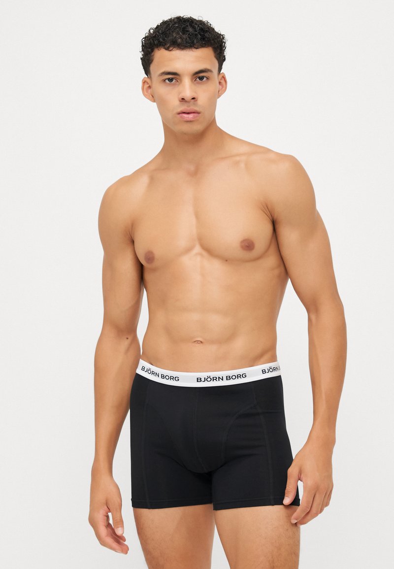 Black boxer shorts with a white waistband featuring "BJÖRN BORG" logo. Smooth texture, fitted design, and mid-thigh length.