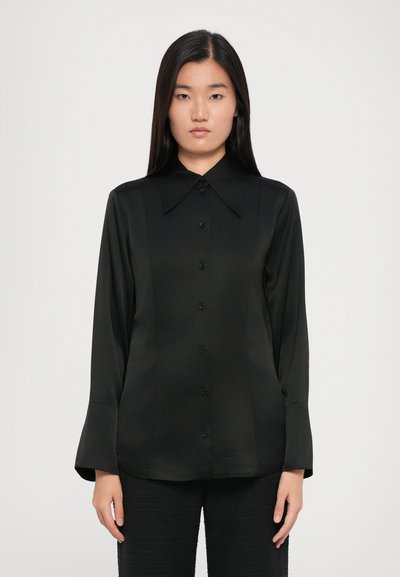 Chemise noire à boutons avec un grand col, des manches longues et une texture de tissu lisse et brillante. Présente des boutons noirs assortis et une coupe ajustée.