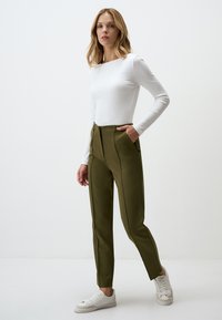 White ribbed long-sleeve top paired with high-waisted olive green trousers featuring front pockets and a tailored fit. White sneakers complete the look.