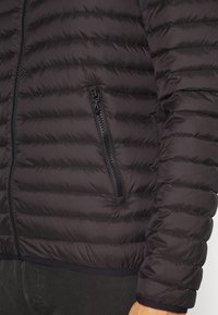 Černá péřová bunda s prošívaným vzorem, viditelným zipem na kapse a elastickými manžetami. Hladká, lehká tkanina s matným povrchem.