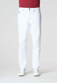 Pantaloni in denim bianco con vestibilità dritta, cinque tasche, chiusura con bottone nero e branding discreto. Indossati con sneakers bianche.