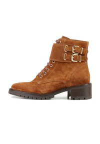 Bottine en daim marron avec un bout arrondi, un laçage à l'avant et deux accents de boucle dorée sur le revers. Talon épais texturé.