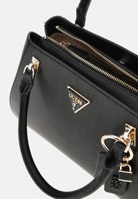 Black textured handbag with gold-tone hardware, double top handles, and a metal logo. Interior features zippered compartments for organization.