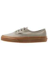 Baskets Vans en toile beige à tige basse avec semelle en caoutchouc marron et lacets, montrant le profil latéral et l'étiquette logo Vans sur le dessus.