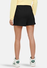 Shorts de sport noirs à texture lisse, dotés d'une taille élastique et de fentes latérales, assortis à des baskets montantes blanches et vertes.