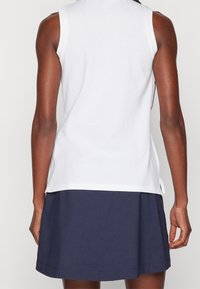 Bílé bezrukávové tričko s rovnými liniemi, spojené s tmavě námořnickou sukní. Tričko má na bocích rozparky blízko lemu pro snadný pohyb.