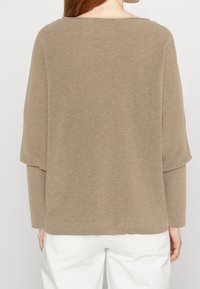 Beige oversized trui van ribstof met een wijde halslijn en verlaagde schoudernaden. Lange mouwen en een relaxte pasvorm.