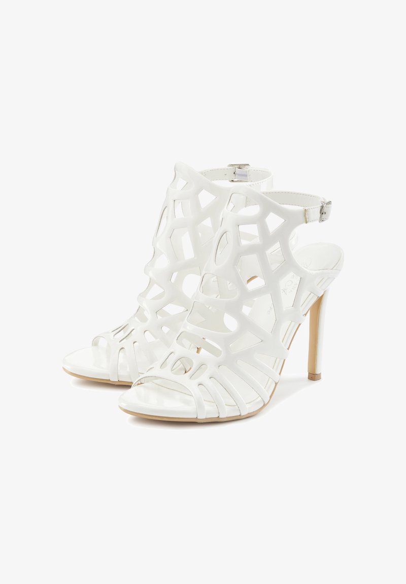 White high-heeled sandals with a cut-out design, glossy finish, open toe, and ankle strap. Heels are slender with a light tan sole accent.