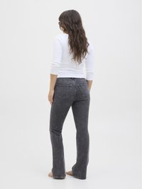 Jeans neri a zampa d'elefante con una finitura sbiadita, design a cinque tasche e vita media. La persona indossa un top bianco attillato.