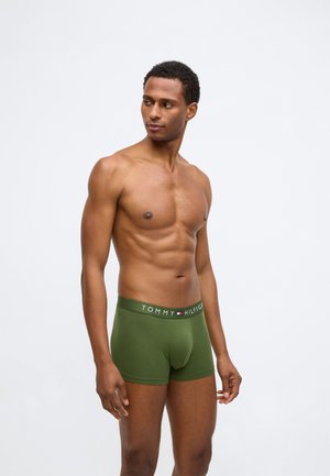 Zelené bavlnené boxerky s brandingom na páske, zobrazené na modeli na neutrálnom pozadí, so priliehavým strihom.
