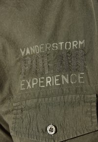 Olivengrünes Stoffhemd mit erhabenem Text "VANDERSTORM POLAR EXPERIENCE". Verfügt über eine Tasche mit einem Metallknopf und einer strukturierten Oberfläche.