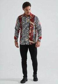 Chemise à manches longues arborant un motif zèbre noir et blanc agrémenté de chaînes rouges et dorées. Design ajusté en tissu léger.