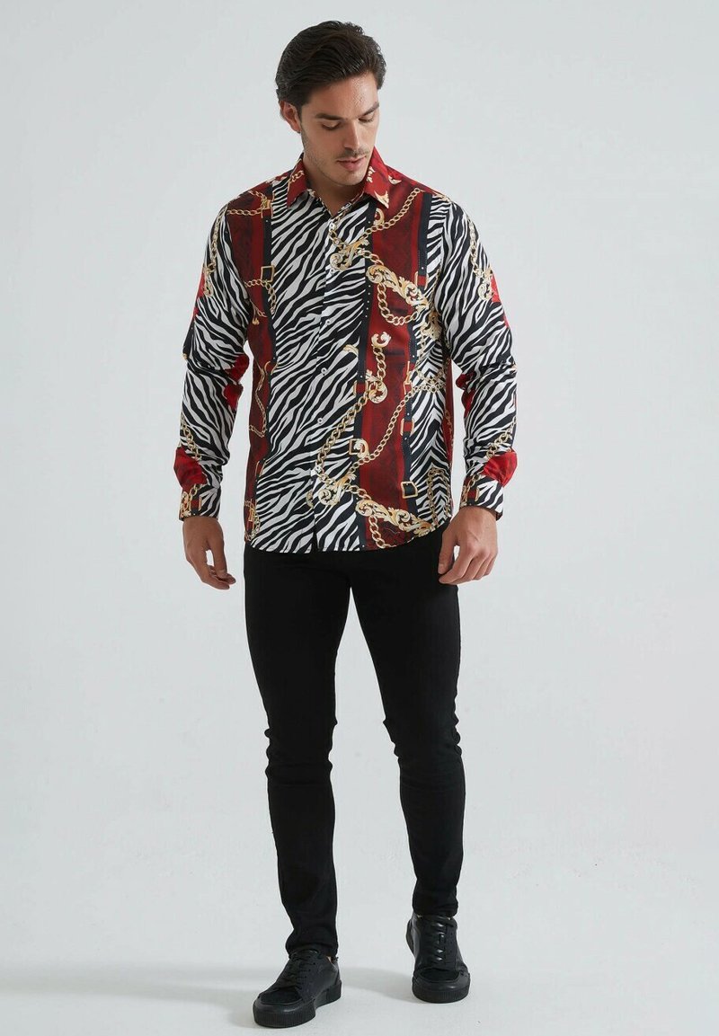 Chemise à manches longues arborant un motif zèbre noir et blanc agrémenté de chaînes rouges et dorées. Design ajusté en tissu léger.