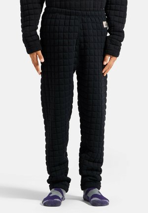 Person wearing black quilted pants and matching top with purple and gray patterned socks on plain background.