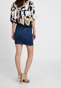 Kortärmad, flerfärgad blus med abstrakt mönster; tillsammans med en mörk denim minikjol och gyllene högklackade sandaler.