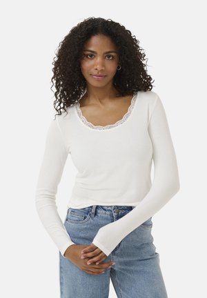 Haut à manches longues blanc avec une texture côtelée et un col en dentelle festonné. Associé à un jean taille haute bleu clair, avec une fermeture à bouton.