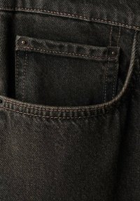 Tejido de mezclilla negra con un pequeño bolsillo frontal y costuras rosas en contraste, con un botón metálico visible y una textura suave.