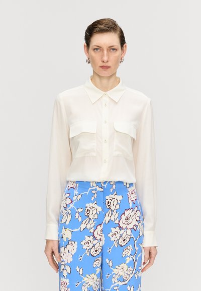Chemise blanche à manches longues, avec deux poches poitrine et un col, associée à un pantalon bleu à motif floral. Tissu lisse et léger.