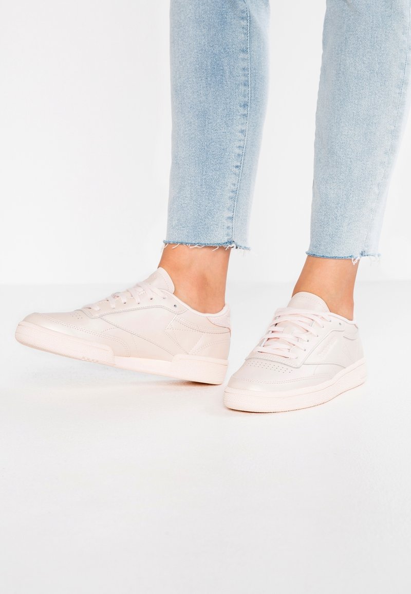 Jasnoróżowe trampki z gładką skórzaną cholewką, perforowanym przodem i płaskimi sznurowadłami. Posiadają gumową podeszwę i subtelne akcenty w designie.