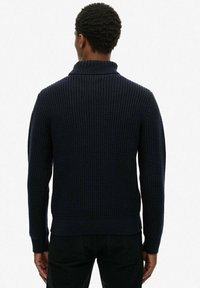 Marineblauer Strickpullover mit geripptem Muster, hohem Kragen und langen Ärmeln. Hat eine enganliegende Passform und ein strukturiertes Rückenmuster.