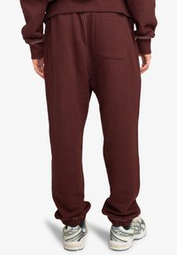 Bordeaux kleurige sweatpants van zacht materiaal, met een achterzak en elastische boorden bij de enkels. Geschikt voor casual kleding.