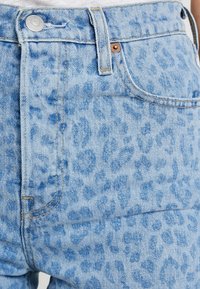 Ljust blå denim, högmidjade jeans med en subtil leopardmönstring, kopparfittings och kontrasterande sömmar. Övre knapp och framficka synliga.