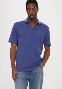 Dark blue polo shirt with a contrasting light blue collar, short sleeves, and an embroidered logo on the chest. Casual fit, cotton material.