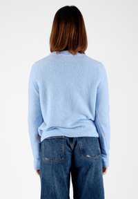 Maglione azzurro chiaro lavorato a maglia con una finitura testurizzata, con scollatura rotonda e maniche lunghe, abbinato a jeans di denim a vita alta.