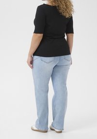 Schwarzes geripptes Oberteil mit kurzen Ärmeln, kombiniert mit hellblauen Schlagjeans. Bemerkenswerte Details sind die gewellten Ärmelsäume und die Gesäßtaschen.