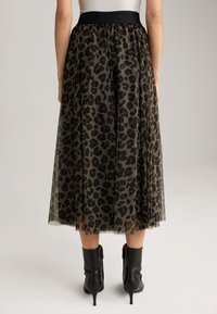 Gonna in tulle con stampa leopardata e vita elastica nera, di lunghezza al polpaccio e con texture a strati. Indossata con stivali neri alla caviglia.