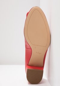 Ballerine en cuir rouge avec un dessus lisse, un bout arrondi et une semelle en caoutchouc texturé avec un petit talon et un marquage sur la semelle extérieure.