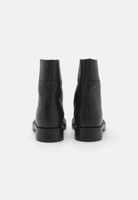 Stivaletti neri in pelle con una texture liscia, design minimalista, punta rotonda e tacco basso a blocco. Le cuciture sono visibili sul retro e sui lati.