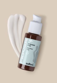 Bruine fles met een witte pomp, gelabeld "FIND PLEASURE AFTER SHAVE FLUID" in lichtblauw. Crèmekleurige vloeistofstreep ernaast op een pastelachtergrond.