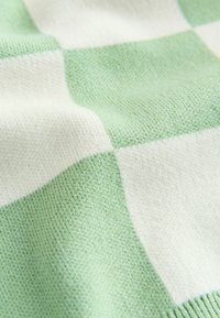 Grün-weißer kariert gestrickter Stoff mit einer weichen Textur, der abwechselnd große Quadrate aus glatten und leicht strukturierten Oberflächen zeigt.