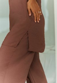 Top e pantaloni in tessuto marrone con una vestibilità ampia, dotati di fessure laterali e maniche corte. Tessuto liscio con dettagli di cucitura sottili.