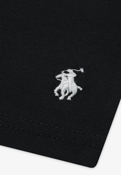 Țesătură neagră cu nervuri, cu un logo alb brodat reprezentând un jucător călare cu un ciocan și un cal, aliniat în colțul din stânga jos.