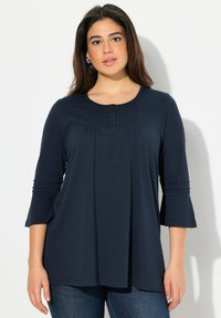 Top blu navy a tre quarti con maniche in tessuto morbido, con parte anteriore plissettata, scollatura rotonda e dettaglio con cinque bottoni al colletto.