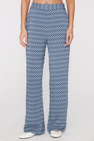 Woman wearing blue patterned loose pants and white shoes standing against a plain background.